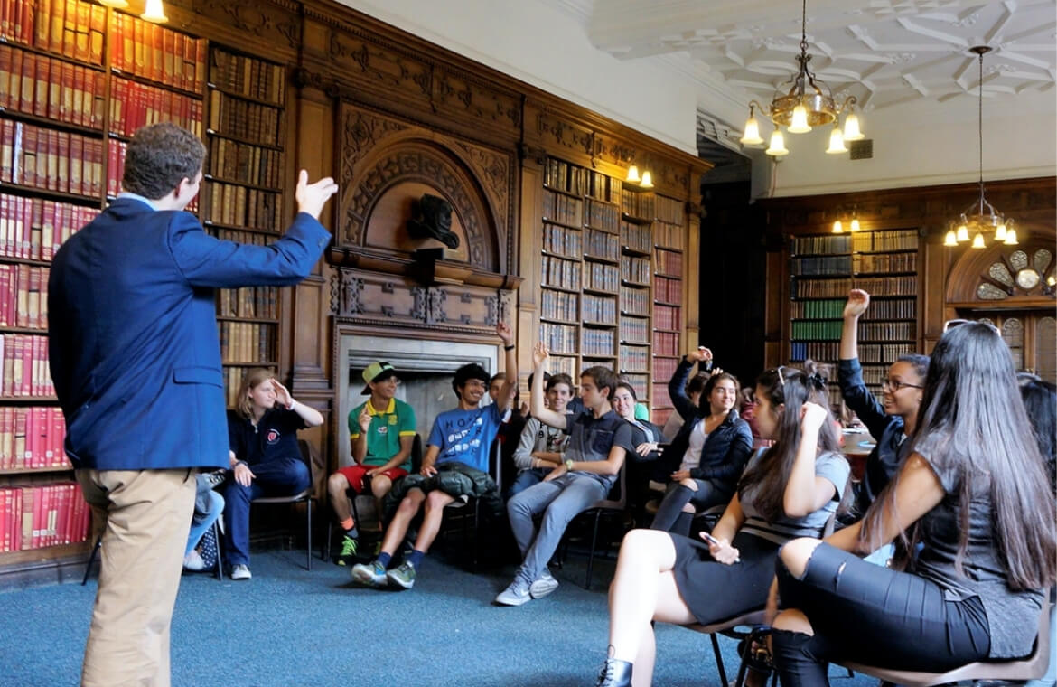 Students and a teacher participating in an Oxford summer school programme in a historic Oxford university classroom