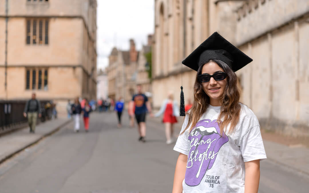 Student in graduation cap stands in Oxford during summer school