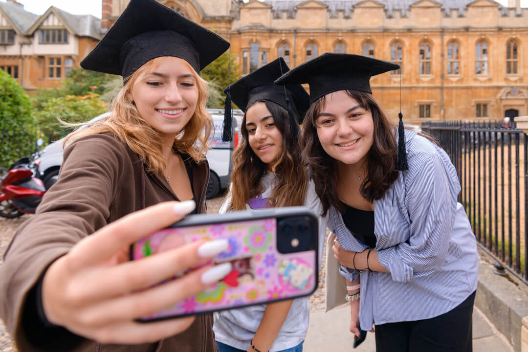 Three Oxford Scholastica Academy summer school students wearing graduation caps, taking a selfie together