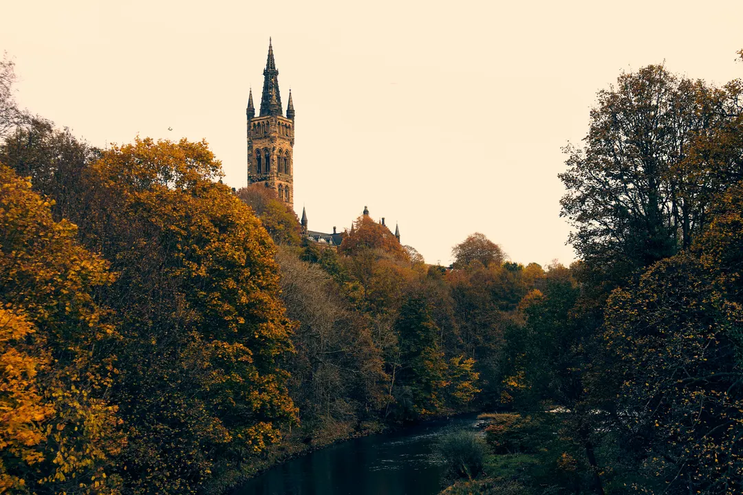 A steeple behind a line of trees and a river in Glasgow