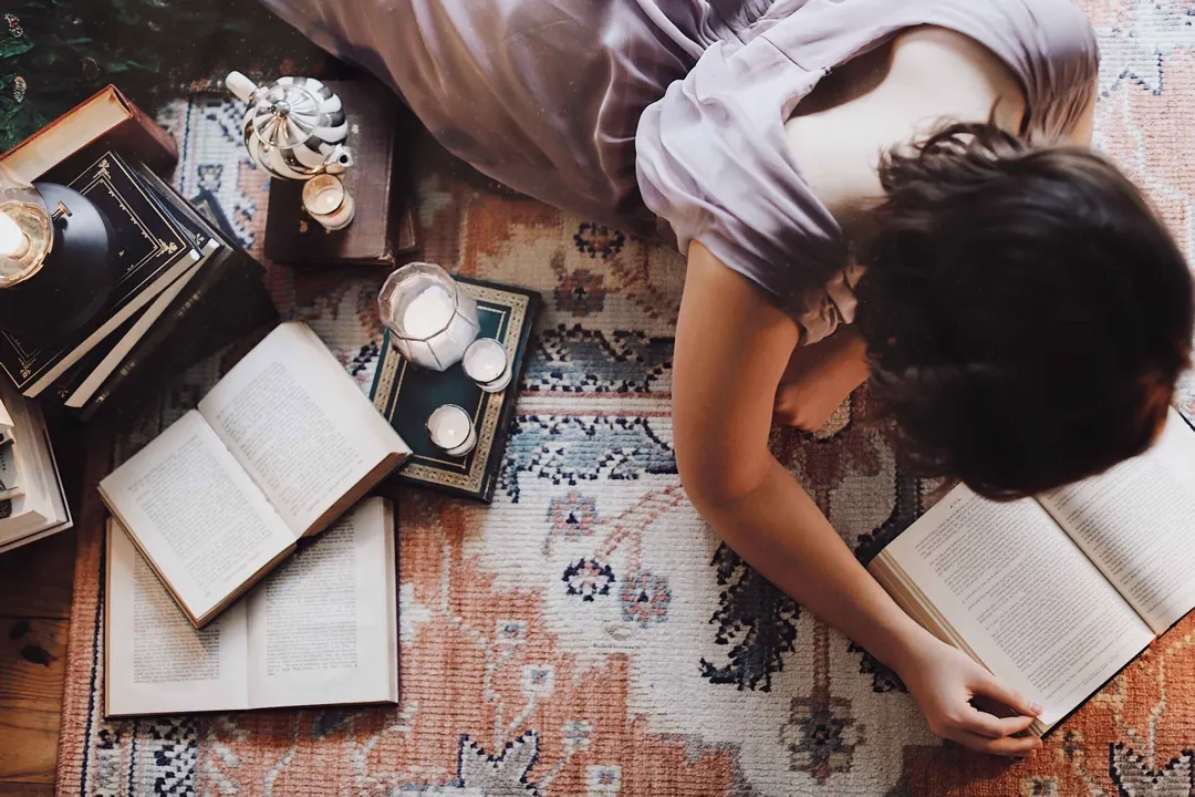 Student lying on floor reading, surrounded by books and candles