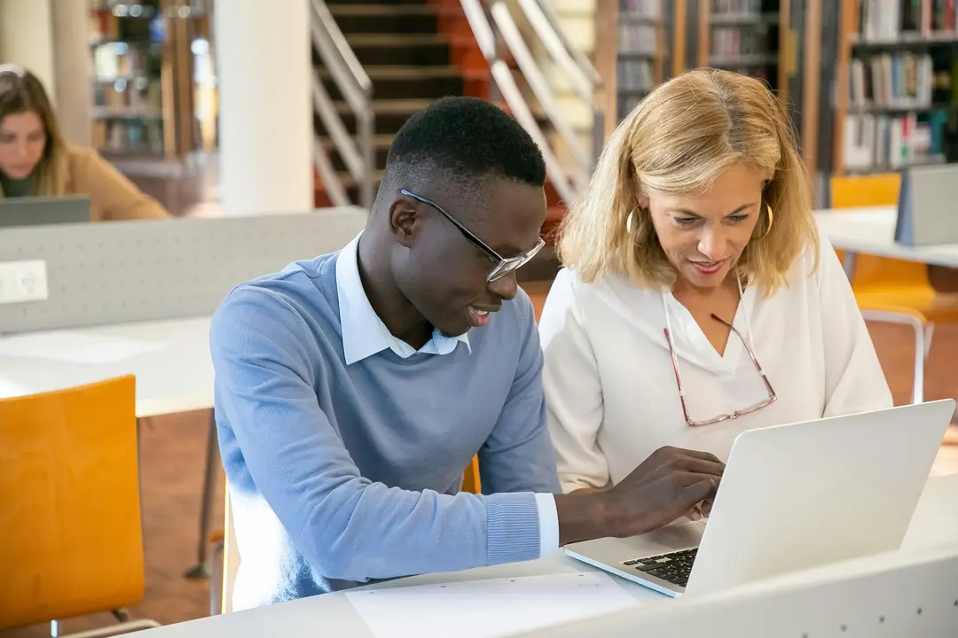 Student and university tutor sitting at a table looking at a laptop screen