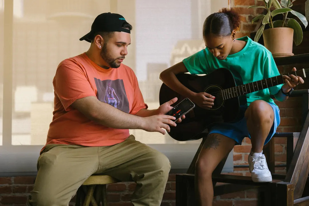 Person playing the guitar, and a second person recording audio on their phone