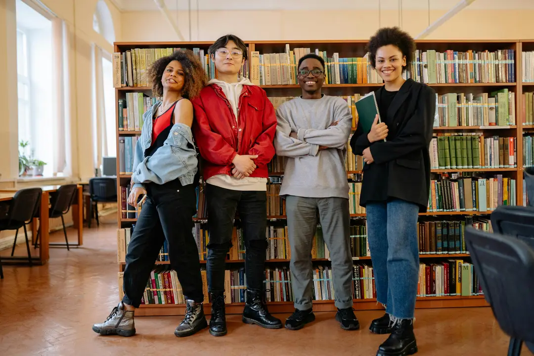 Four students standing in front of a bookshelf, smiling