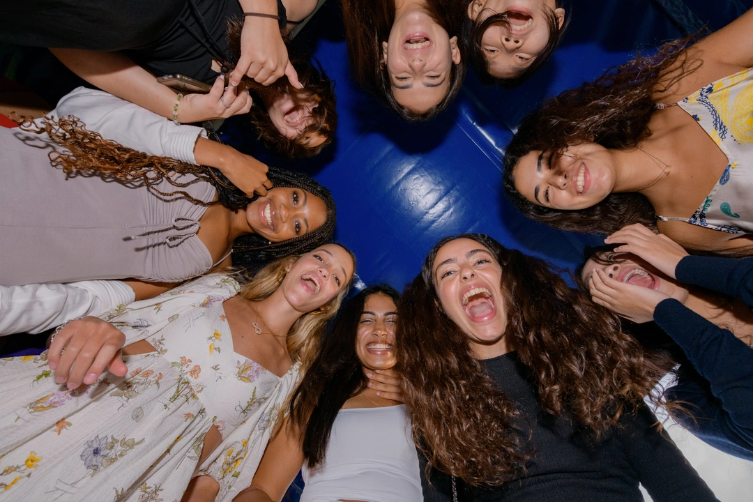 Group of students in a circle, looking down and smiling at the camera