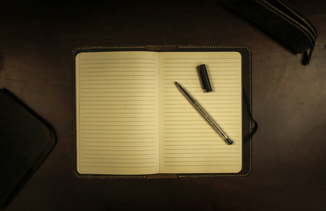 A pen and notebook lying flat on a dark background