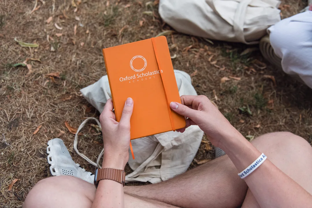 Close up of a person holding an orange notebook with the Oxford Scholastica logo on the front cover